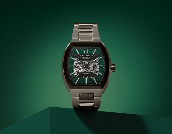 Bulova Maquina automatic watch with tonneau-shaped case and green skeleton dial on green background.
